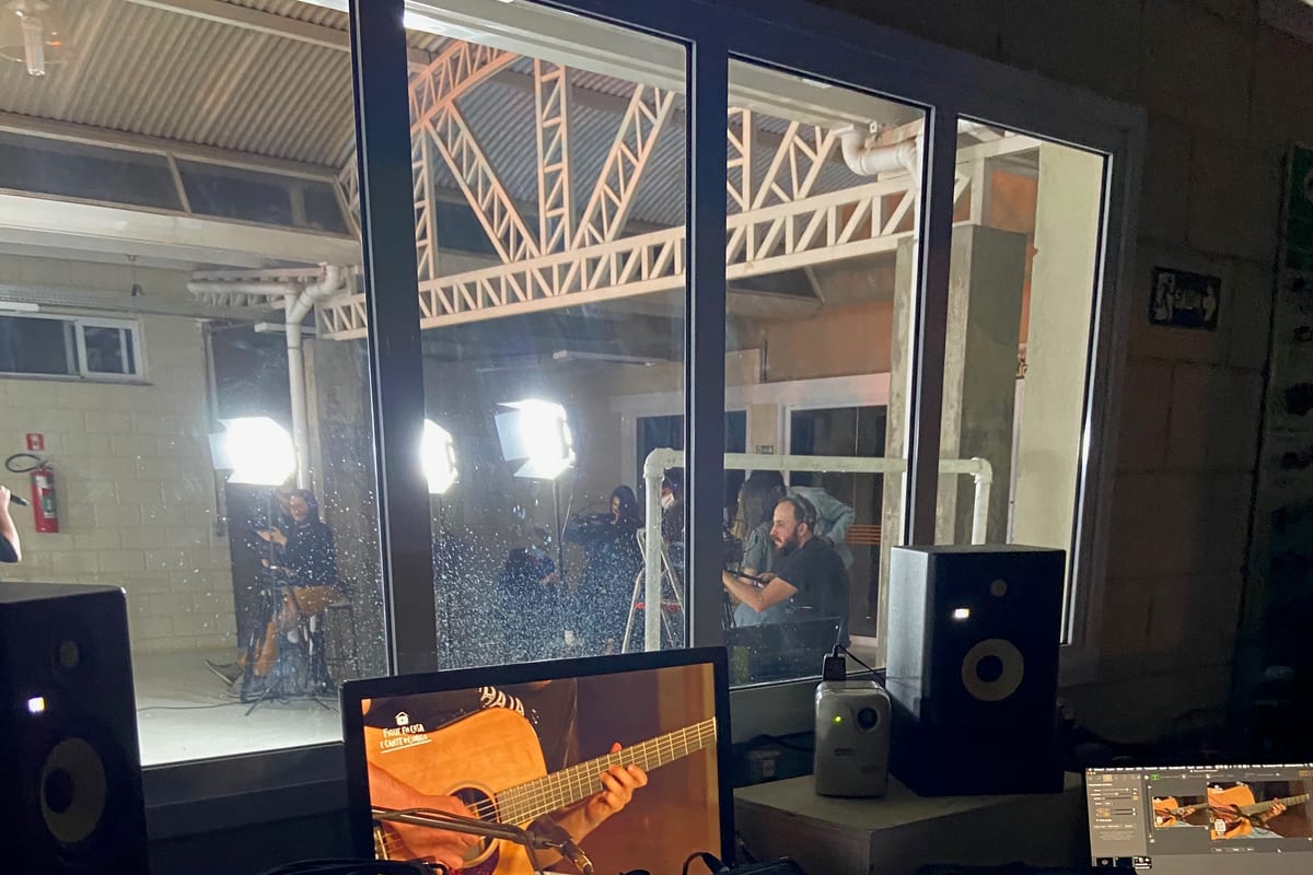 FOH position during a COVID-era livestream — operator at the console under low house light, broadcast monitors glowing, empty room beyond.