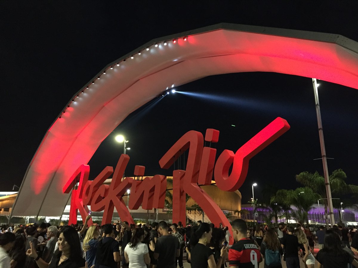 The illuminated red 'Rock in Rio' arch over the festival gate at night, crowds streaming in beneath it.